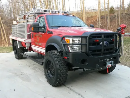 Exterior view of small fire truck showing cab, body compartments, and wheel/tire area.