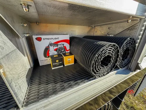 Compartment shelf close-up with boxed tool and rolled black mats.