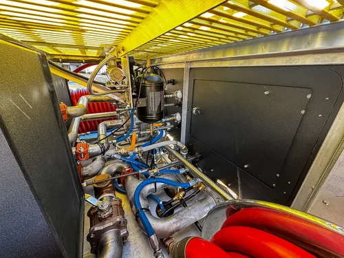 Pump compartment close-up with valves, pipes, and red hose reel at right.