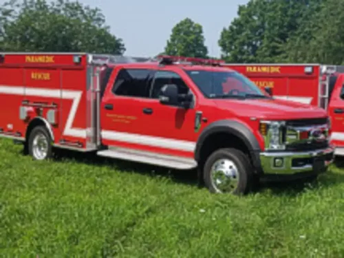 Exterior view of small fire truck showing cab, body compartments, and wheel/tire area.