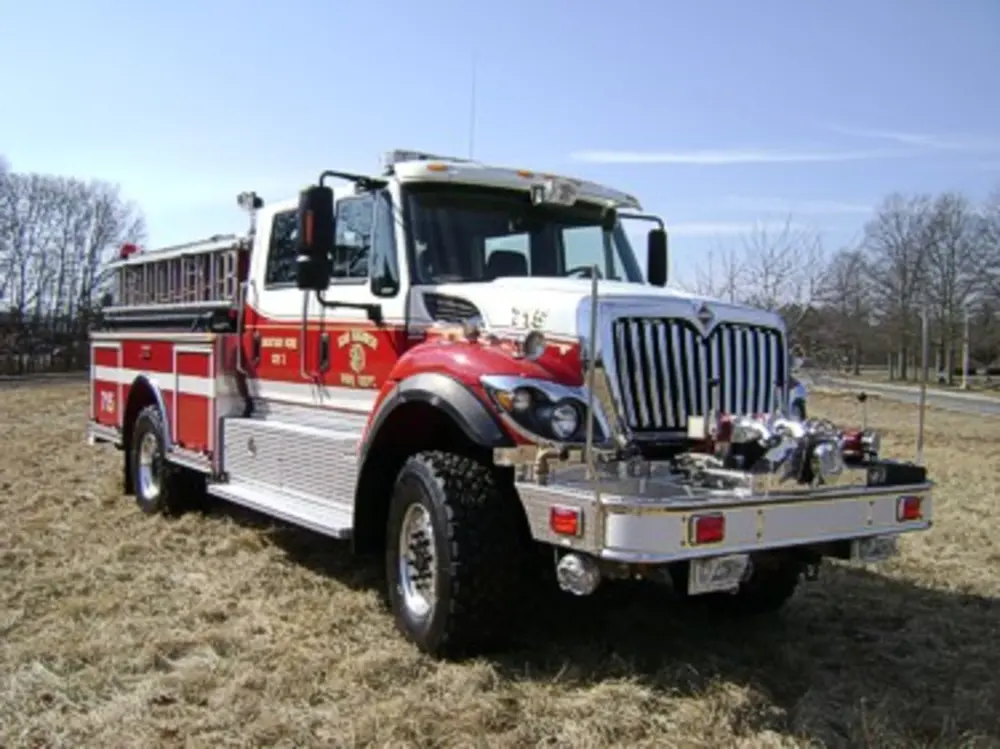 Exterior view of small fire truck showing cab, body compartments, and wheel/tire area.