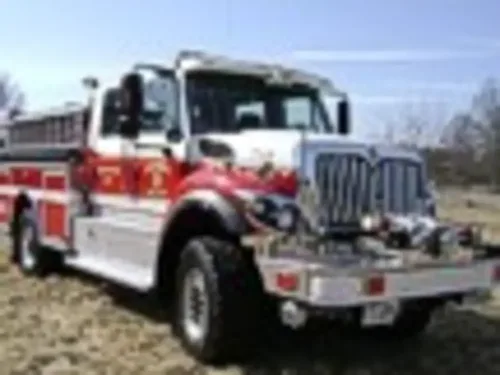 Exterior view of small fire truck showing cab, body compartments, and wheel/tire area.