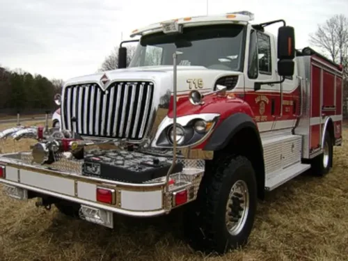 Exterior view of small fire truck showing cab, body compartments, and wheel/tire area.