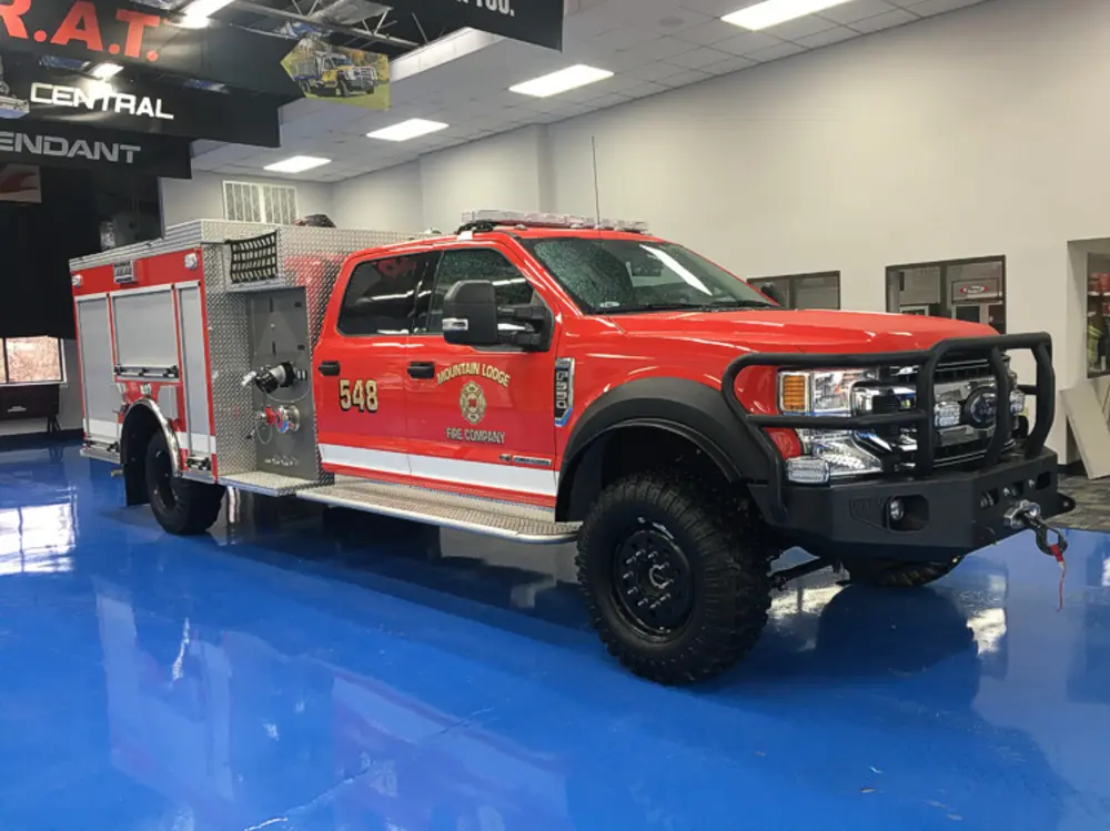 Exterior view of small fire truck showing cab, body compartments, and wheel/tire area.
