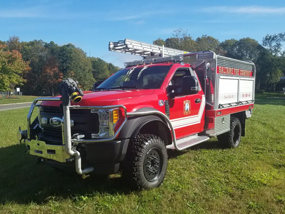 Exterior view of small fire truck showing cab, body compartments, and wheel/tire area.