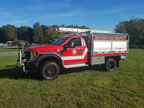 Exterior view of small fire truck showing cab, body compartments, and wheel/tire area.