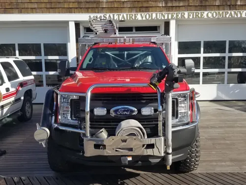 Exterior view of small fire truck showing cab, body compartments, and wheel/tire area.