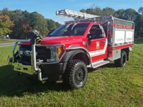 Exterior view of small fire truck showing cab, body compartments, and wheel/tire area.