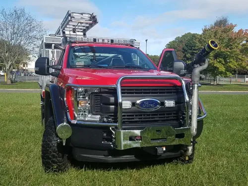 Exterior view of small fire truck showing cab, body compartments, and wheel/tire area.