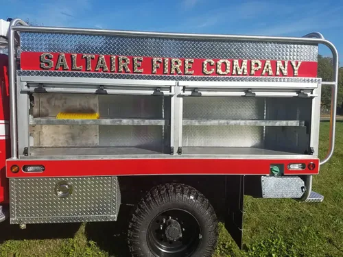 Exterior view of small fire truck showing cab, body compartments, and wheel/tire area.