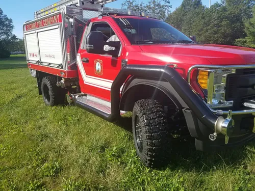Exterior view of small fire truck showing cab, body compartments, and wheel/tire area.