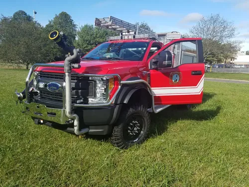 Exterior view of small fire truck showing cab, body compartments, and wheel/tire area.