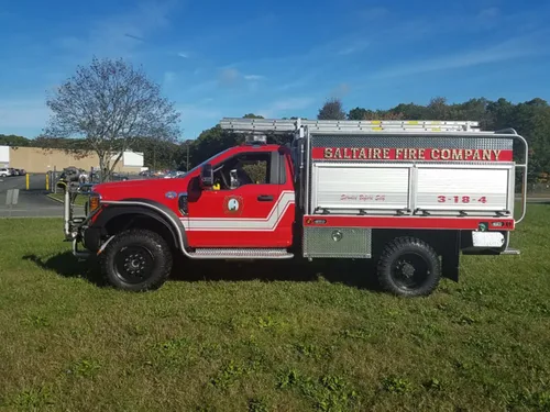 Exterior view of small fire truck showing cab, body compartments, and wheel/tire area.