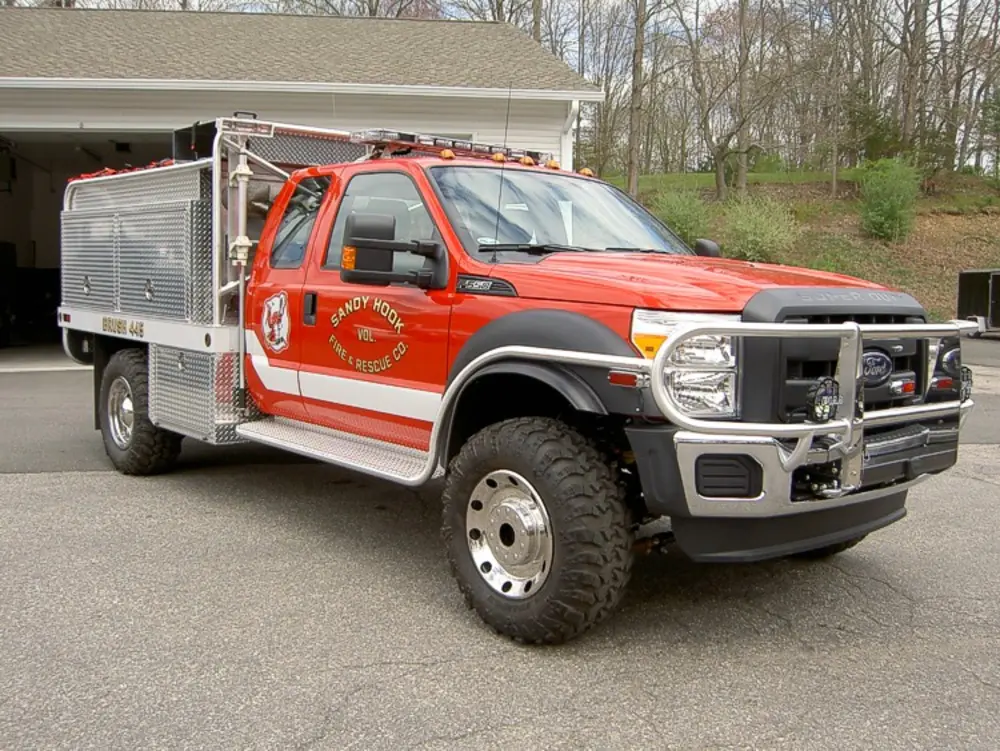 Exterior view of small fire truck showing cab, body compartments, and wheel/tire area.