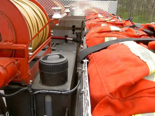 Exterior view of small fire truck showing cab, body compartments, and wheel/tire area.