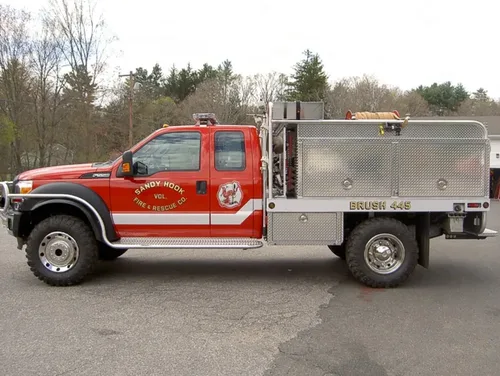Exterior view of small fire truck showing cab, body compartments, and wheel/tire area.
