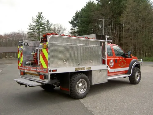 Exterior view of small fire truck showing cab, body compartments, and wheel/tire area.