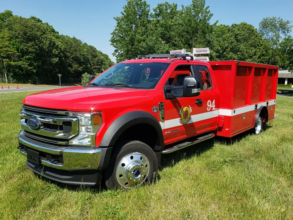 Exterior view of small fire truck showing cab, body compartments, and wheel/tire area.