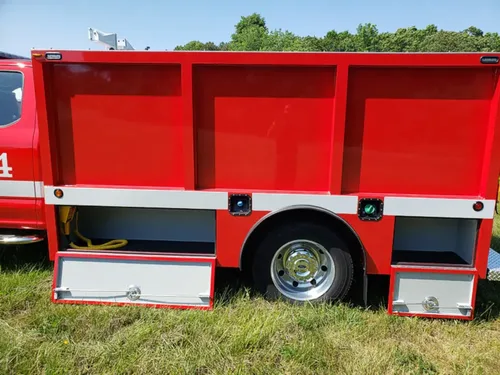 Exterior view of small fire truck showing cab, body compartments, and wheel/tire area.