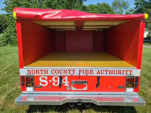 Exterior view of small fire truck showing cab, body compartments, and wheel/tire area.