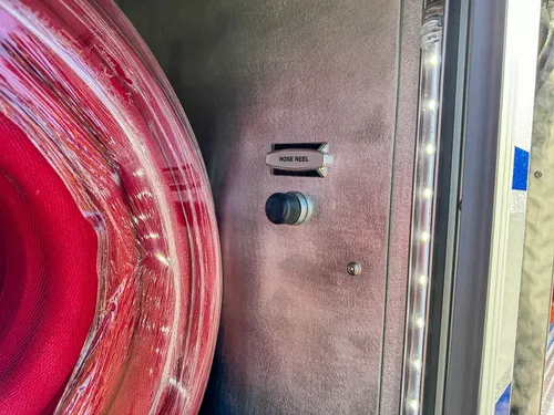 Close-up of red coiled hose inside side storage compartment.
