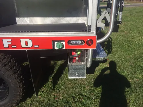 Exterior view of small fire truck showing cab, body compartments, and wheel/tire area.