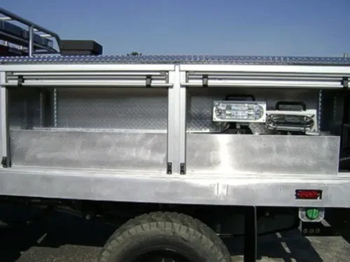 Exterior view of small fire truck showing cab, body compartments, and wheel/tire area.