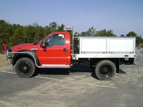 Exterior view of small fire truck showing cab, body compartments, and wheel/tire area.