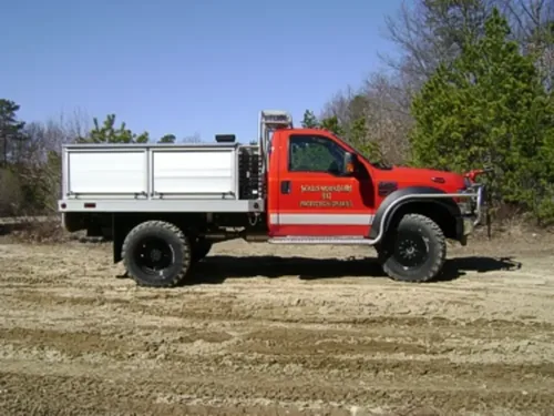 Exterior view of small fire truck showing cab, body compartments, and wheel/tire area.