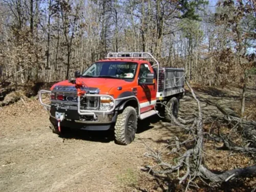 Exterior view of small fire truck showing cab, body compartments, and wheel/tire area.