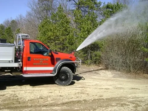 Exterior view of small fire truck showing cab, body compartments, and wheel/tire area.