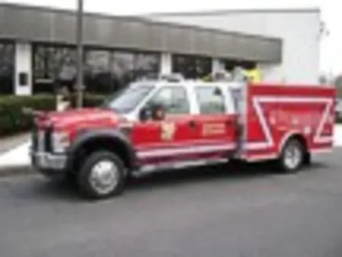 Exterior view of small fire truck showing cab, body compartments, and wheel/tire area.