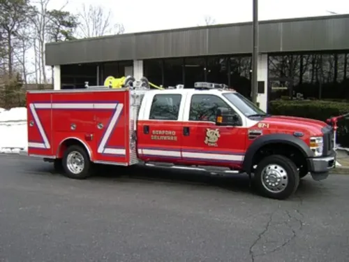 Exterior view of small fire truck showing cab, body compartments, and wheel/tire area.
