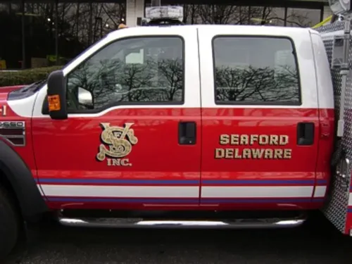 Exterior view of small fire truck showing cab, body compartments, and wheel/tire area.