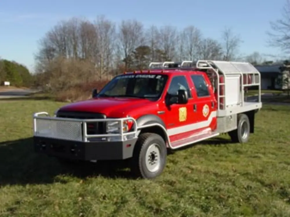 Exterior view of small fire truck showing cab, body compartments, and wheel/tire area.