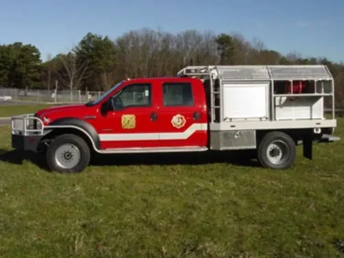 Exterior view of small fire truck showing cab, body compartments, and wheel/tire area.