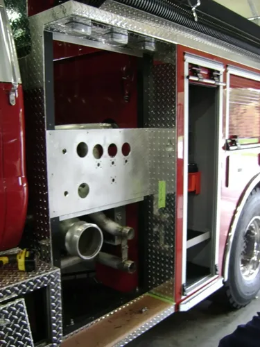 Exterior view of small fire truck showing cab, body compartments, and wheel/tire area.