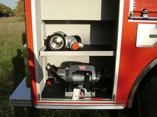 Exterior view of small fire truck showing cab, body compartments, and wheel/tire area.