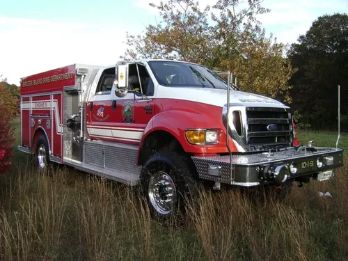 Exterior view of small fire truck showing cab, body compartments, and wheel/tire area.