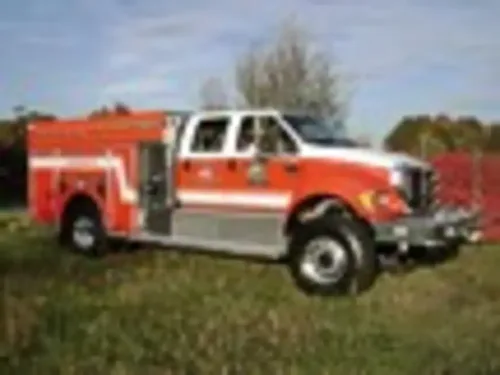 Exterior view of small fire truck showing cab, body compartments, and wheel/tire area.