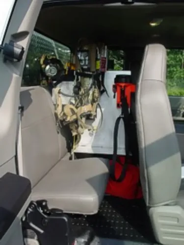 Exterior view of small fire truck showing cab, body compartments, and wheel/tire area.