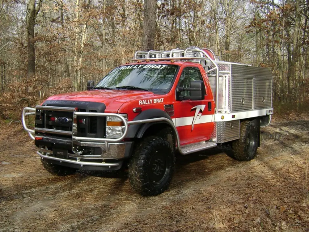 Exterior view of small fire truck showing cab, body compartments, and wheel/tire area.