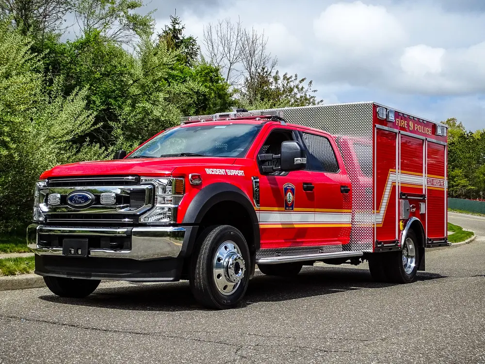 Exterior view of small fire truck showing cab, body compartments, and wheel/tire area.