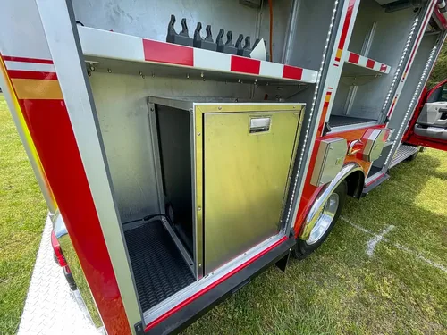 Exterior view of small fire truck showing cab, body compartments, and wheel/tire area.