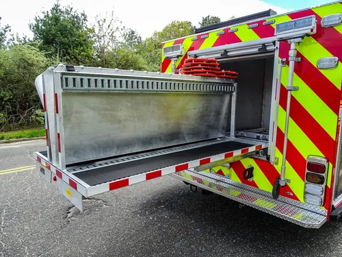 Exterior view of small fire truck showing cab, body compartments, and wheel/tire area.