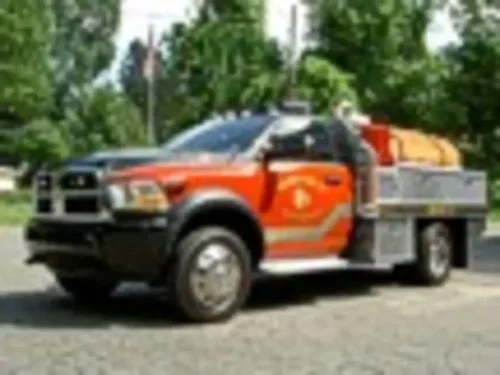 Exterior view of small fire truck showing cab, body compartments, and wheel/tire area.