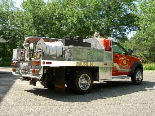 Exterior view of small fire truck showing cab, body compartments, and wheel/tire area.