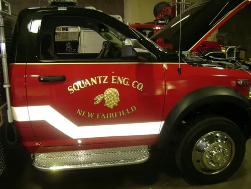 Exterior view of small fire truck showing cab, body compartments, and wheel/tire area.