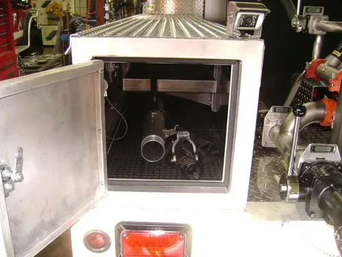Exterior view of small fire truck showing cab, body compartments, and wheel/tire area.