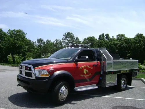 Exterior view of small fire truck showing cab, body compartments, and wheel/tire area.